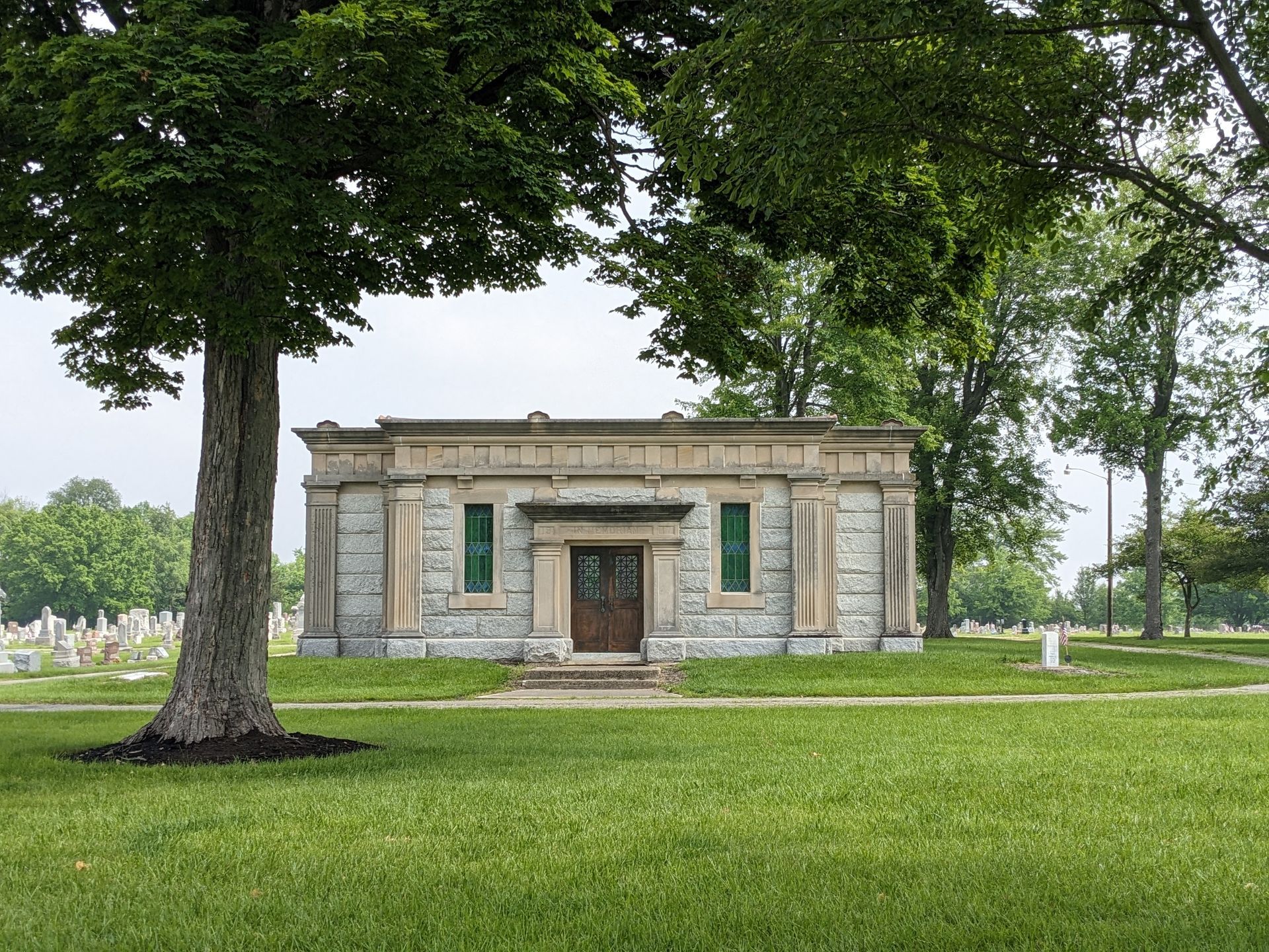 Stone mausoleum in a cemetery, framed by trees and green grass.