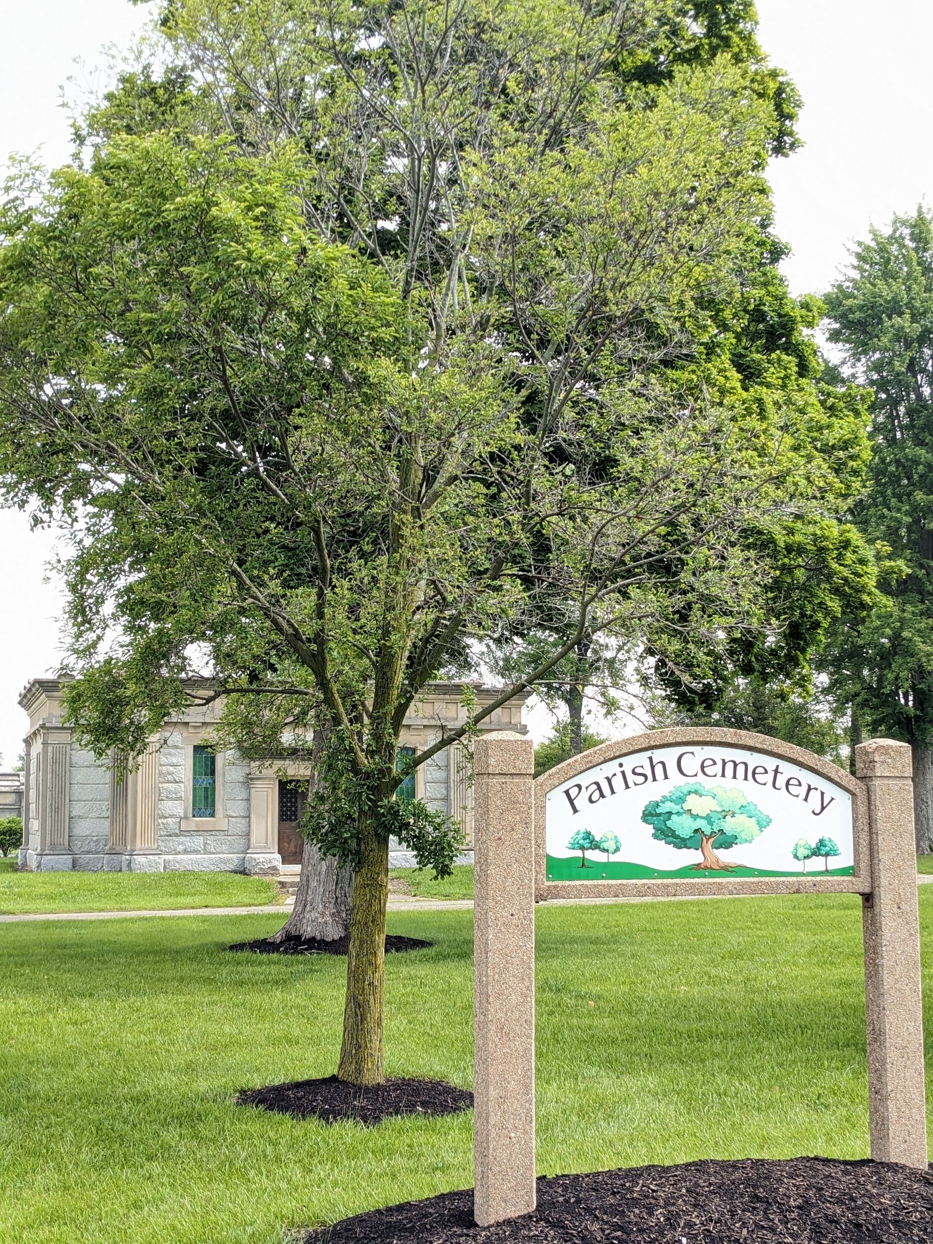 Sign for Parish Cemetery with building and tree in the background on a sunny day.