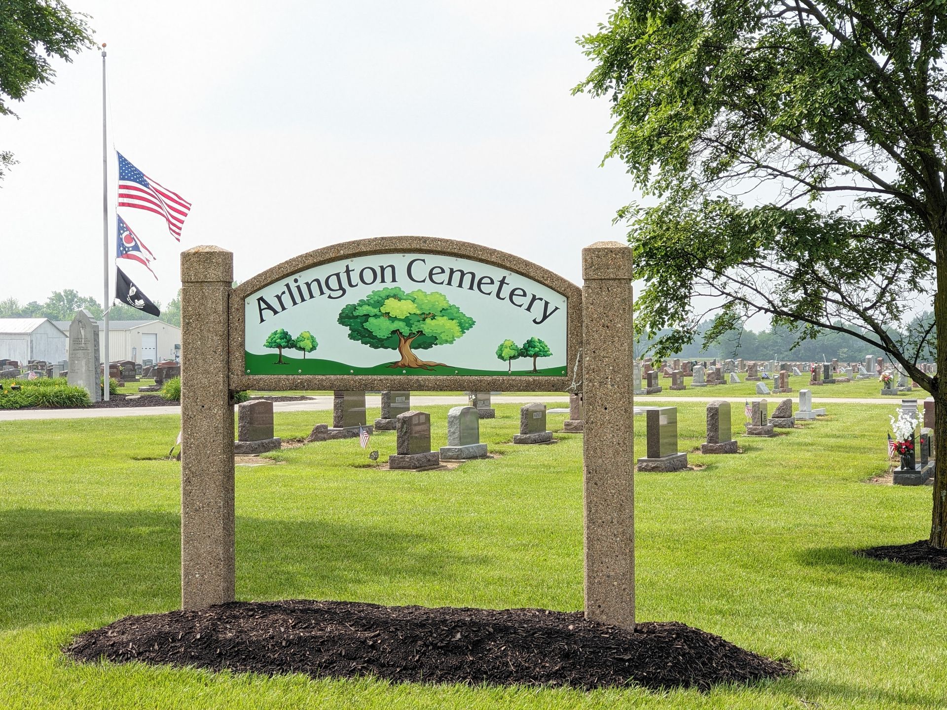 Sign for Arlington Cemetery, with green grass, headstones, and flags in the background.