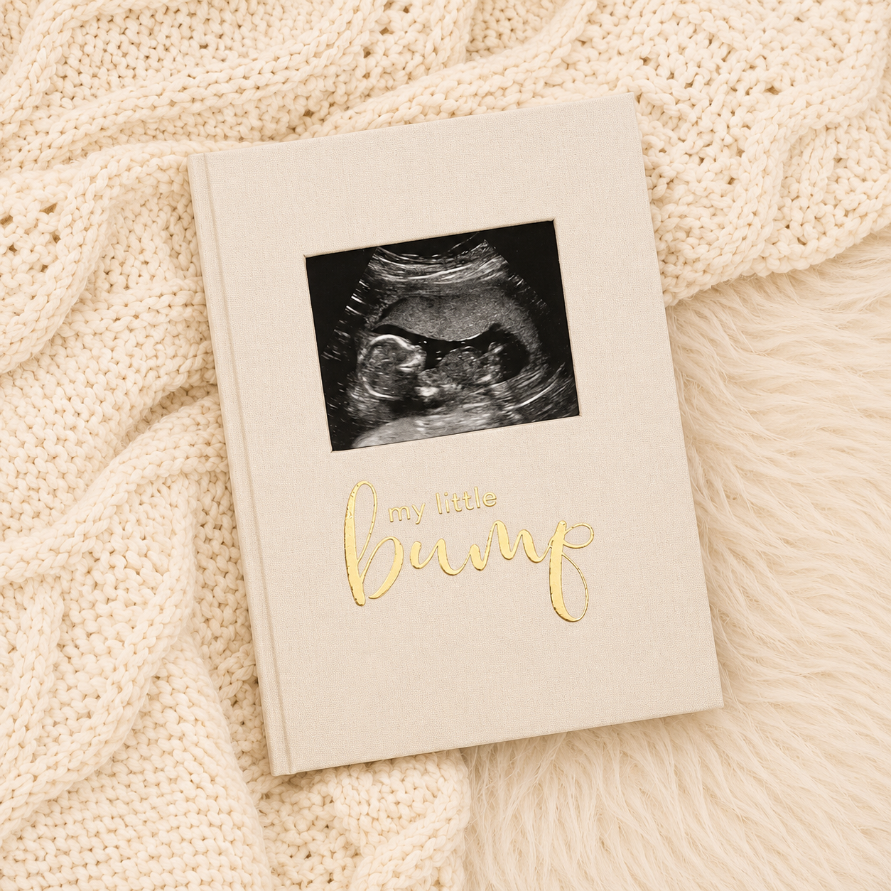 White baby announcement card with ultrasound photo and gold “coming soon” text on a cream knitted blanket