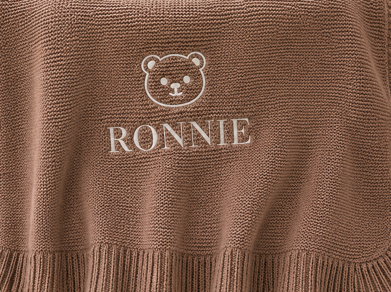 Brown ribbed fabric with an embroidered bear face and the name “RONNIE” underneath.