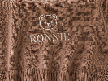 Brown knit fabric with an embroidered bear face and the name “RONNIE” below it.