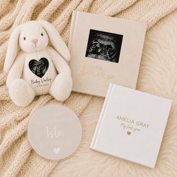 Gift set with plush bunny, ultrasound photo, candle, and white keepsake boxes on a beige blanket