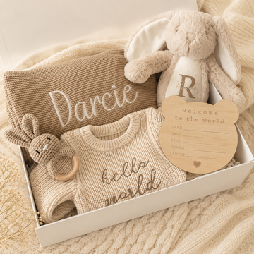 Gift basket with a personalized bunny plush, knitted blanket, and baby clothes in neutral beige tones