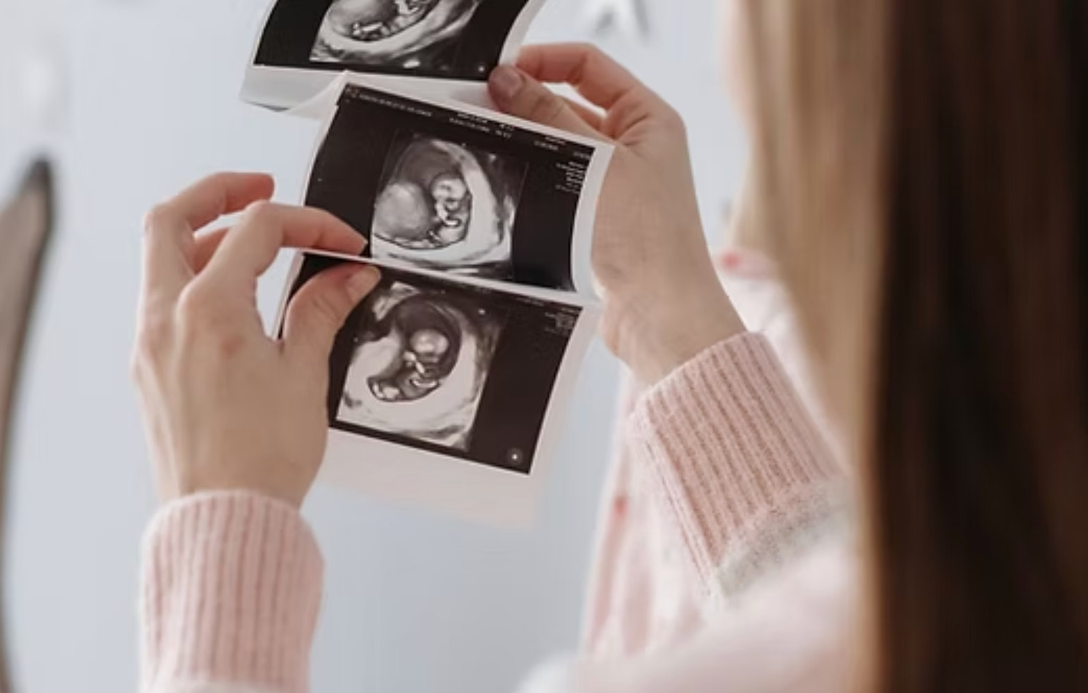 Hands holding ultrasound scan photos in a softly lit room