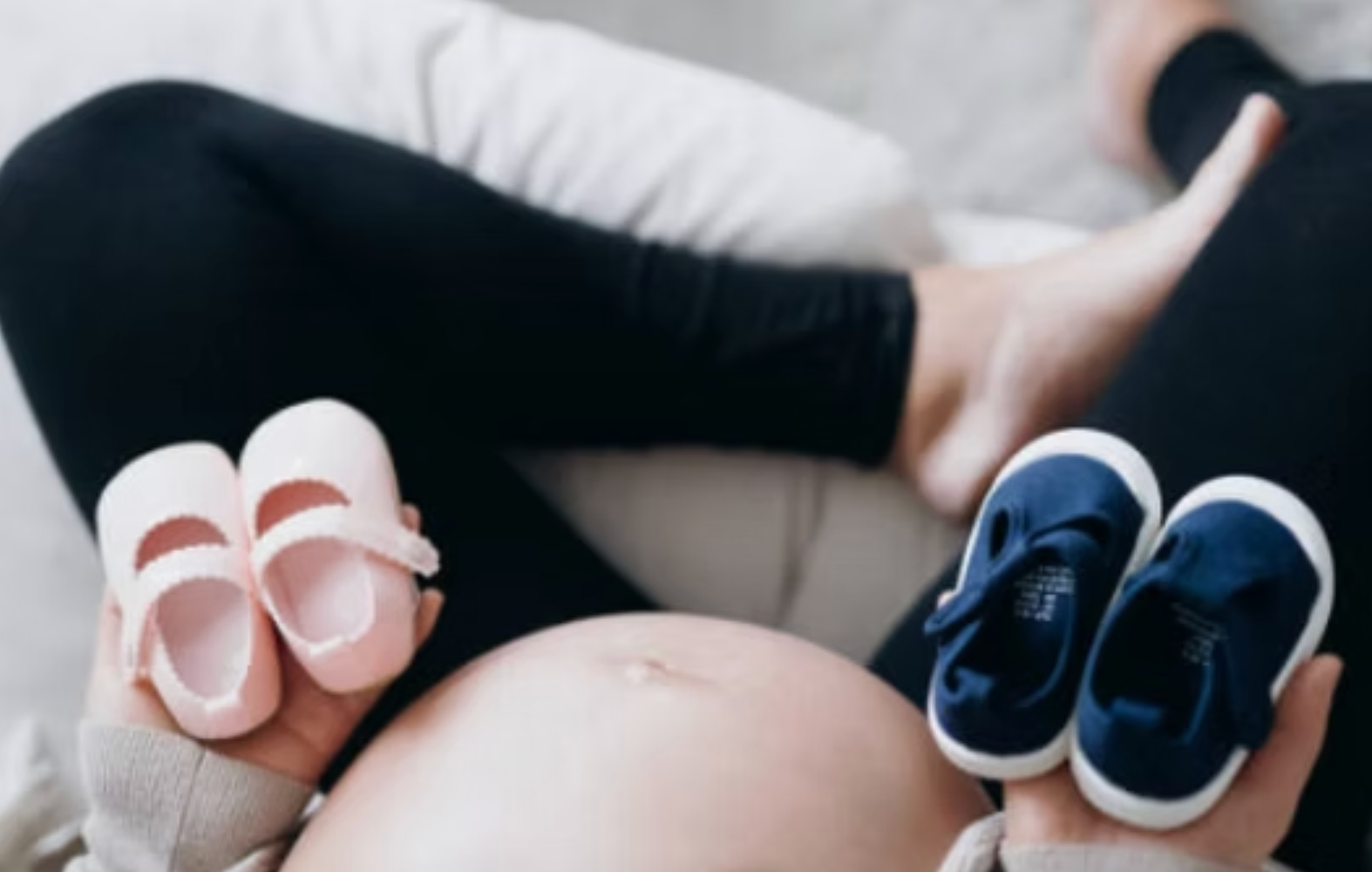 Baby bump with tiny pink and blue shoes on a bed