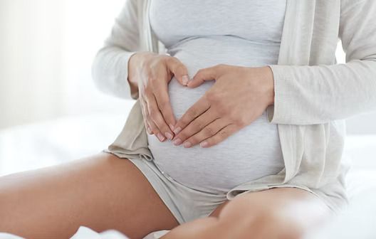 Pregnant person resting hands on belly in white clothing