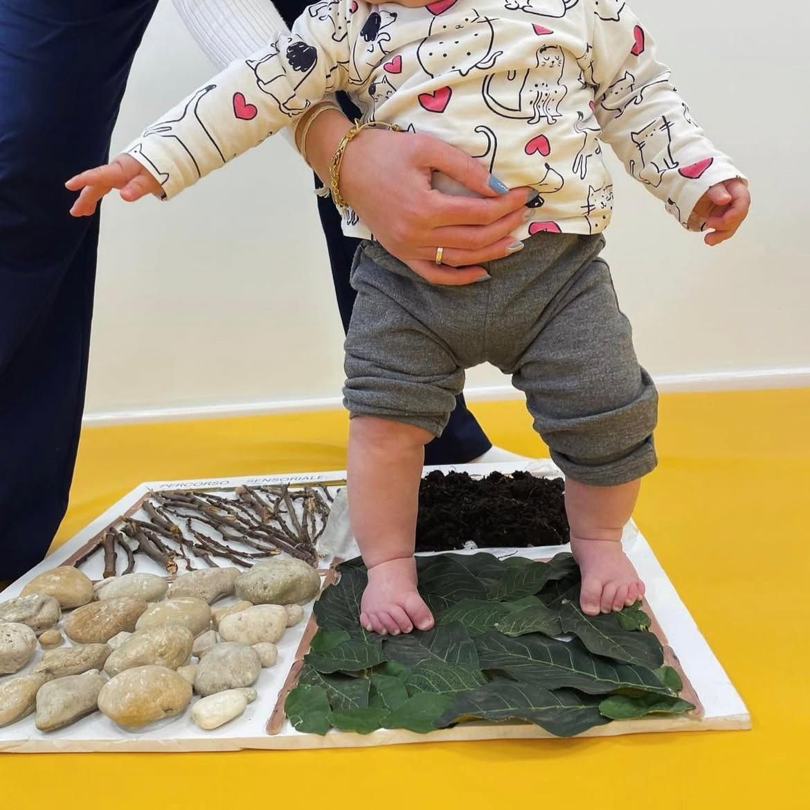 Un bambino è in piedi su un tappetino con pietre e foglie