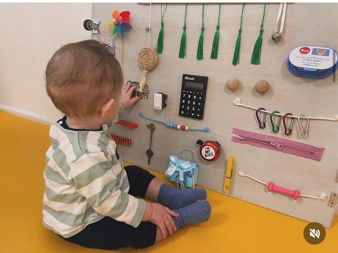 Un bambino è seduto sul pavimento e gioca con un pannello sensoriale