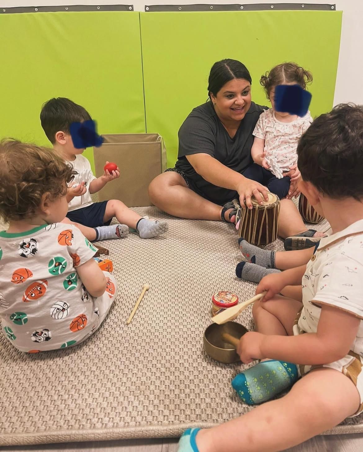 Una donna è seduta sul pavimento insieme a un gruppo di bambini che suonano strumenti musicali.