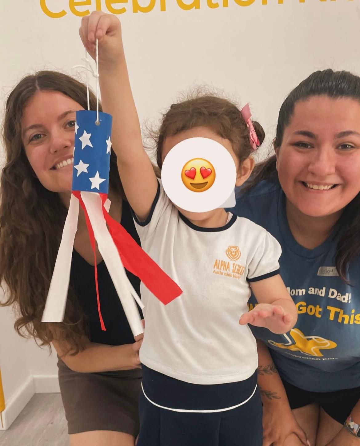Una bambina con una faccina sorridente sul viso è tenuta in braccio da due donne