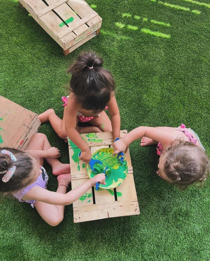 Tre bambine sono sedute sull'erba e giocano con la vernice.