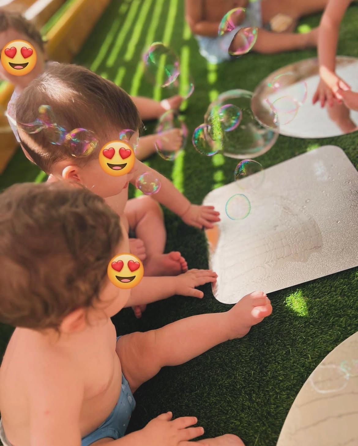 Un gruppo di bambini è seduto sull'erba e gioca con le bolle di sapone