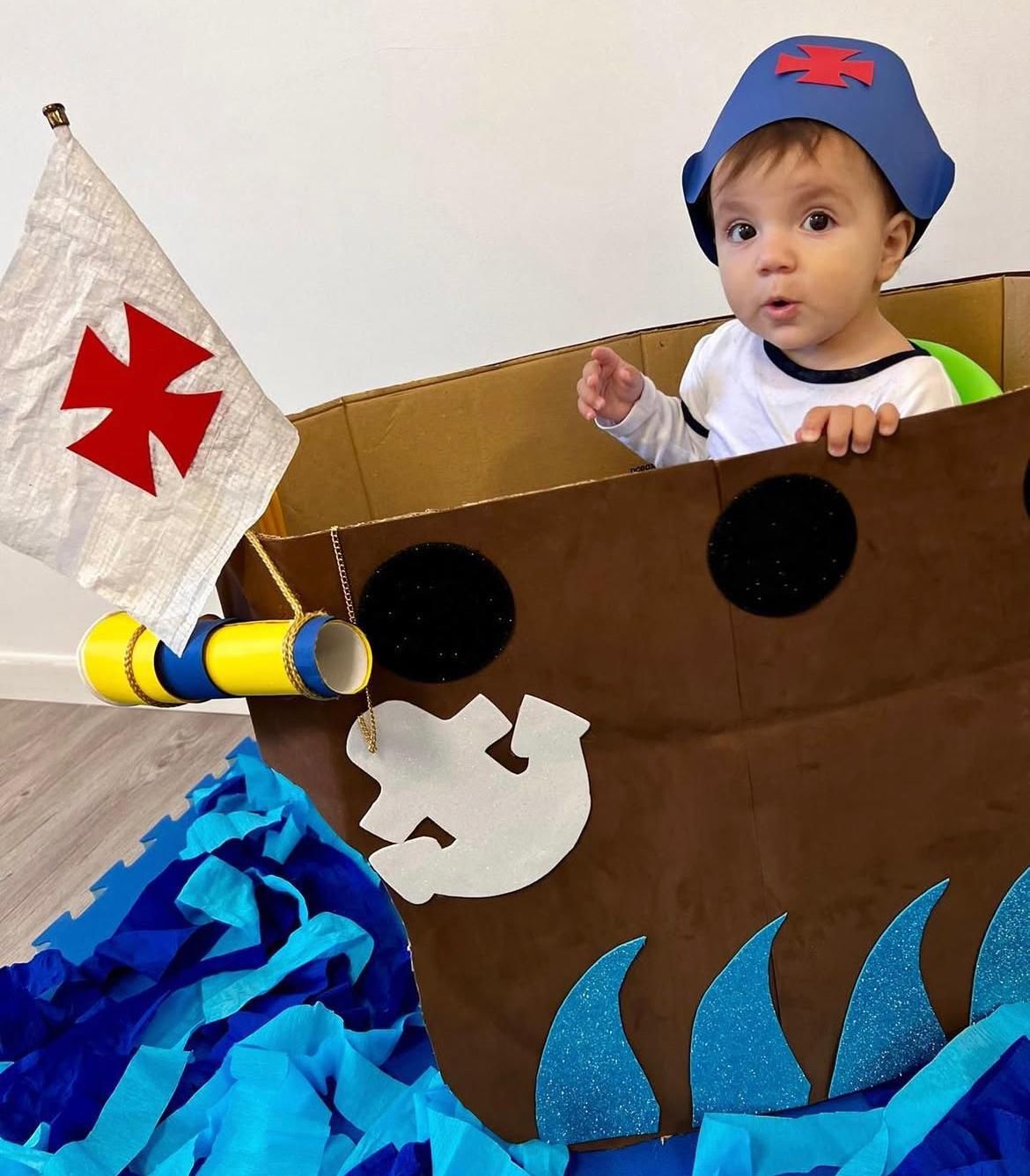 Un bambino con un cappello da pirata è seduto su una barca di cartone