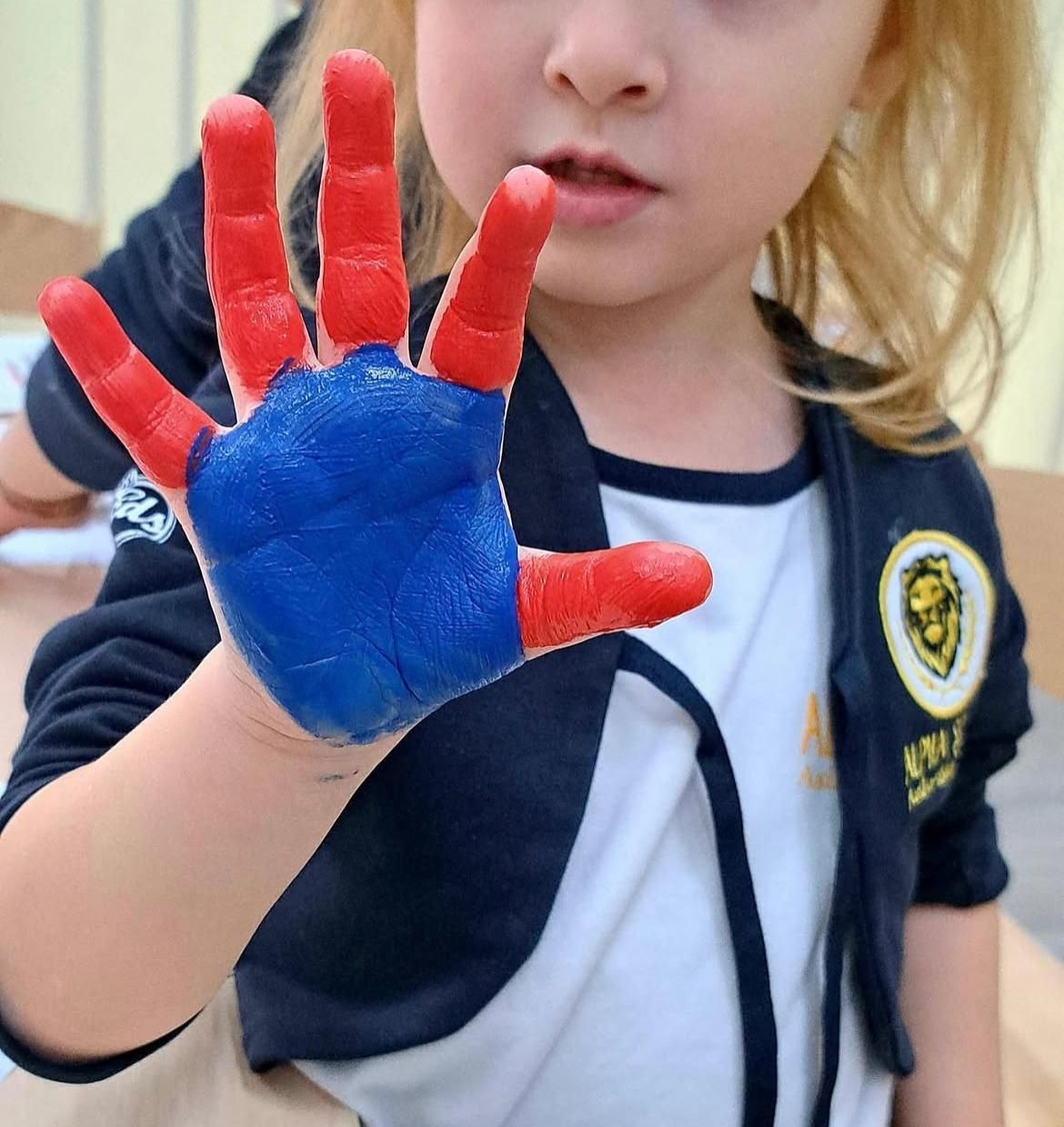 Una bambina con vernice rossa e blu sulle mani