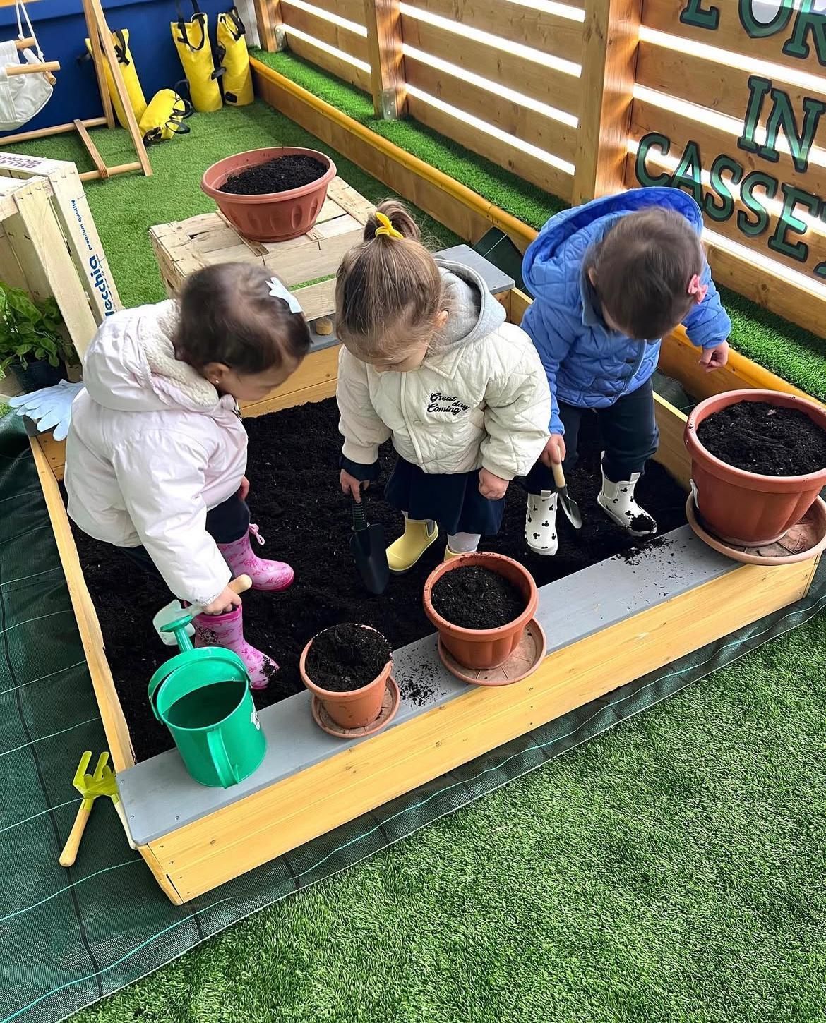Tre bambini stanno giocando in una sabbiera con delle piante in vaso.