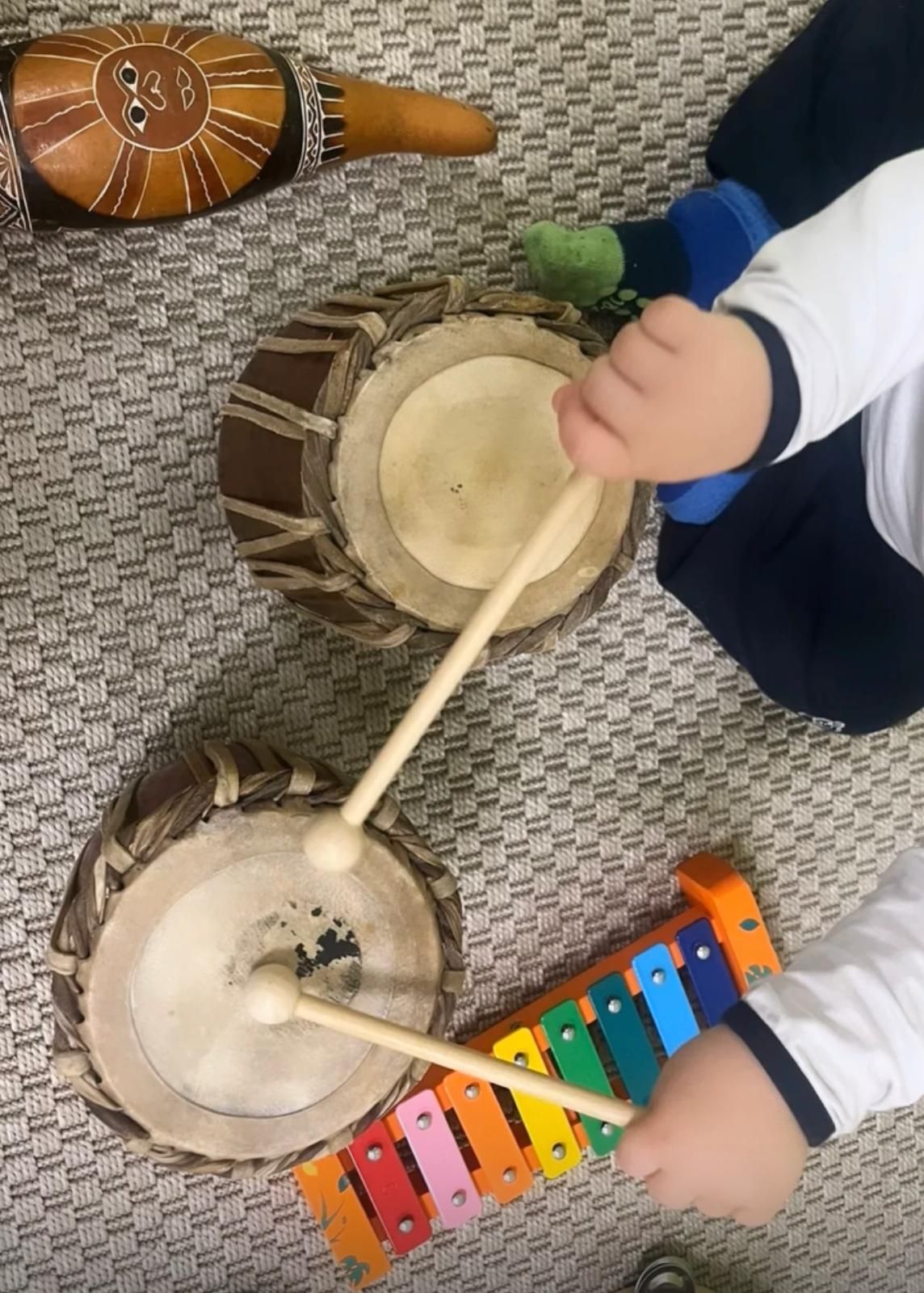Un bambino suona un tamburo e uno xilofono sul pavimento.