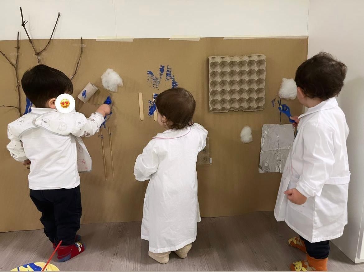 Tre bambini in camice bianco sono in piedi davanti a un muro di cartone.