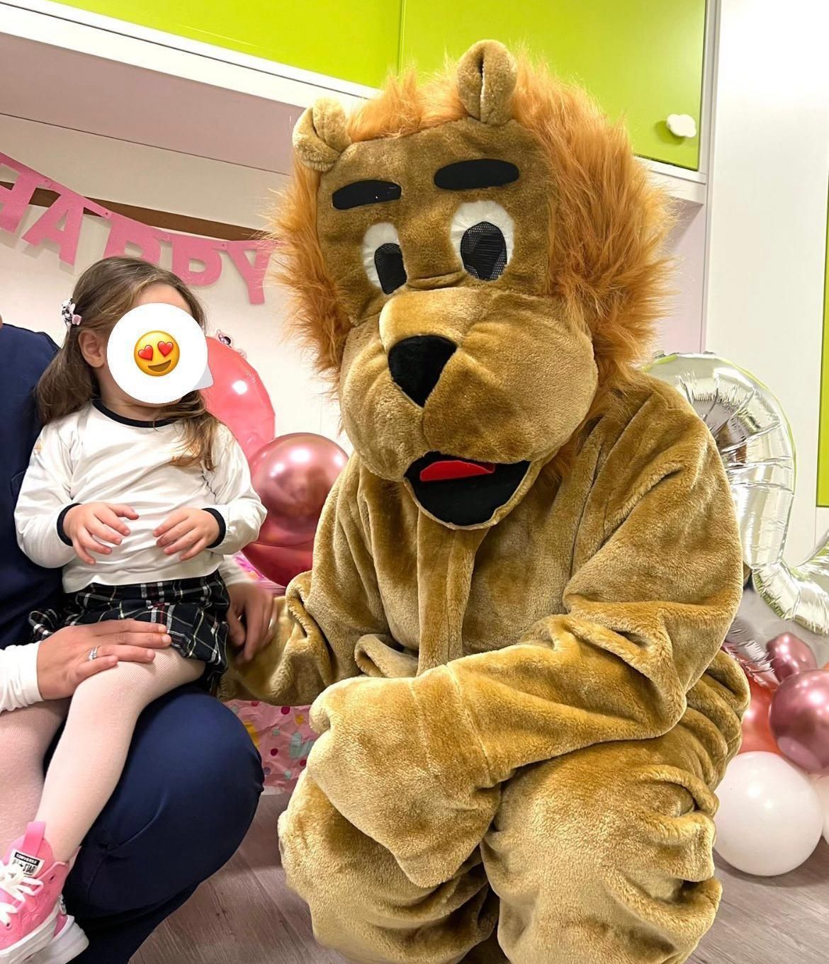 Una mascotte leone è seduta accanto a una bambina