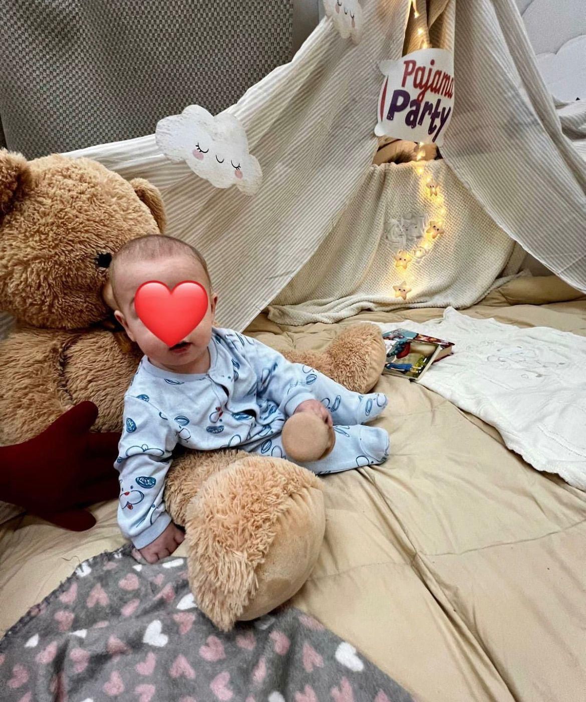 Un bambino è seduto su un letto accanto a un orsacchiotto.