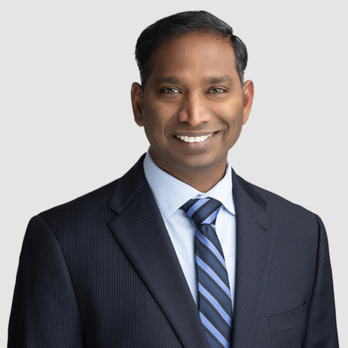 Jitender Sunke in suit smiling, with striped tie against light background.