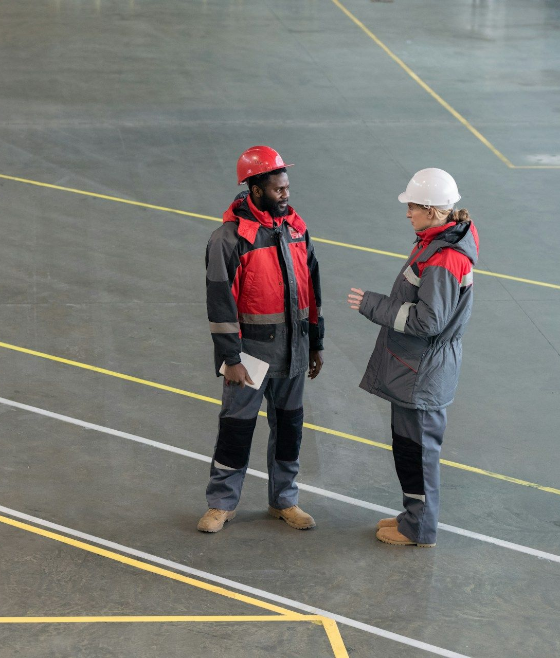 Two people having a conversation in a warehouse, both wearing hardhats.