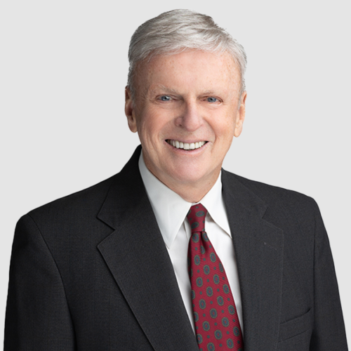 Fred Holland in a black suit smiles, wearing a red patterned tie.