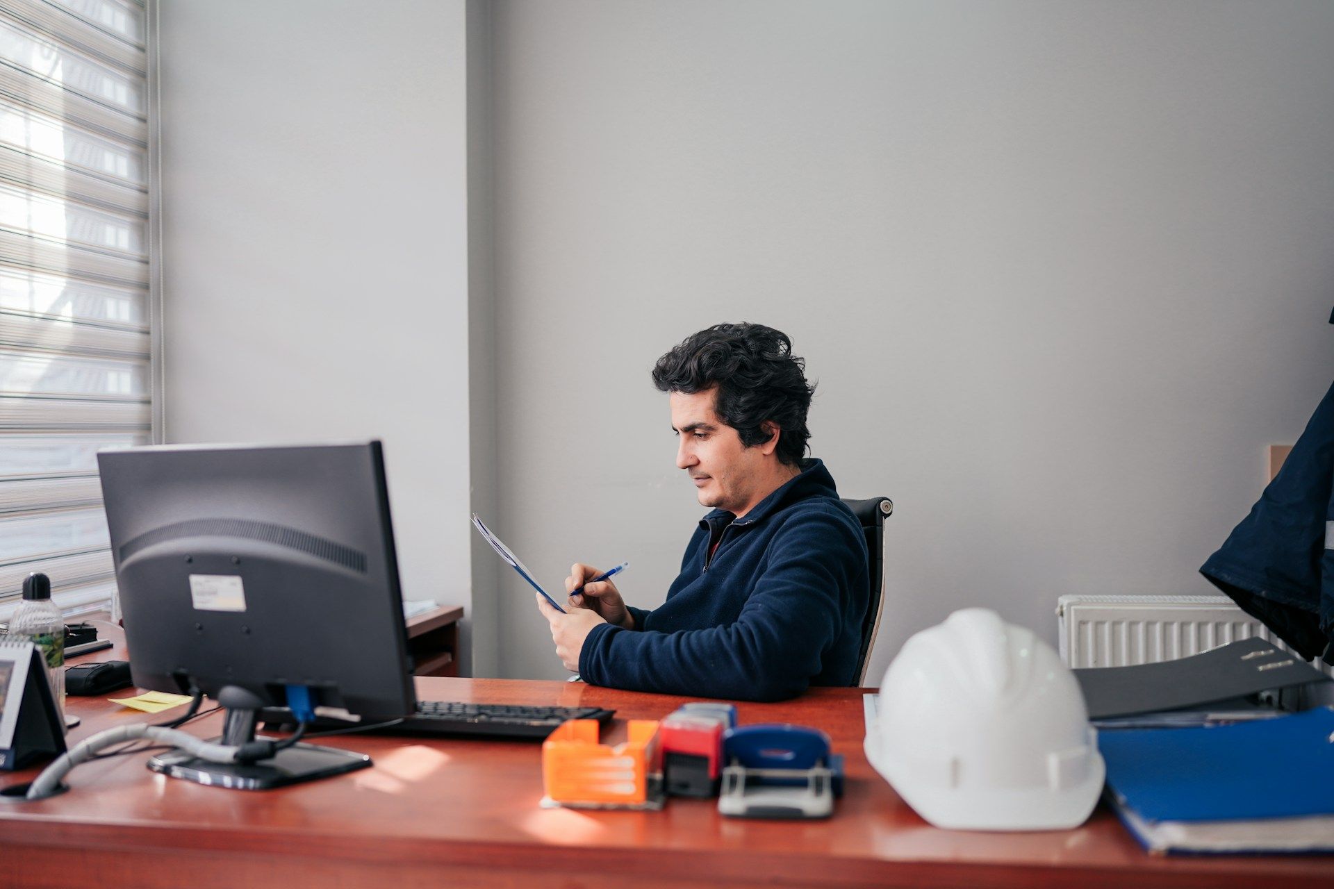 Man reviewing papers near his computer in a brightly lit office.