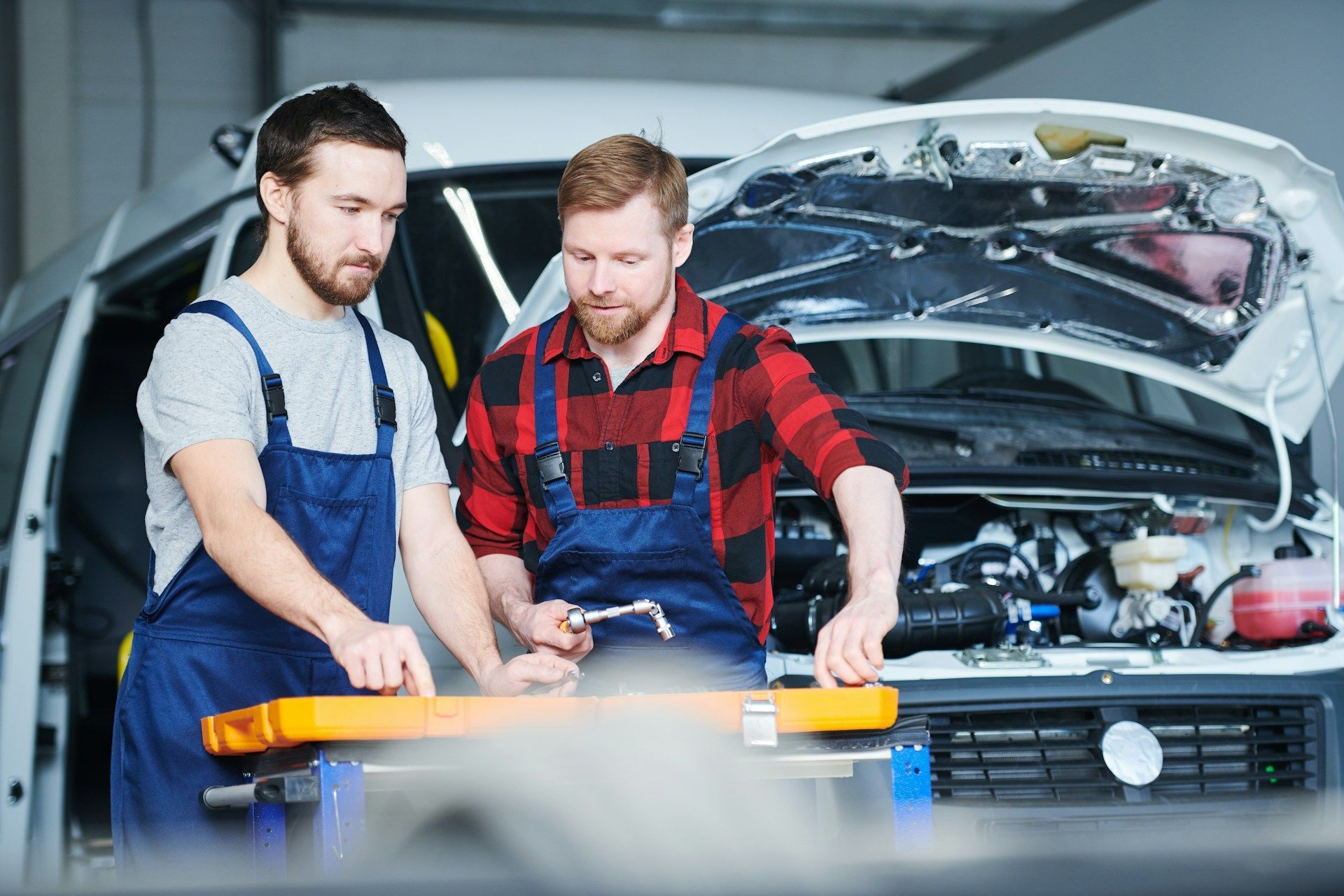 Two mechanics examining their tools in front of a white van
