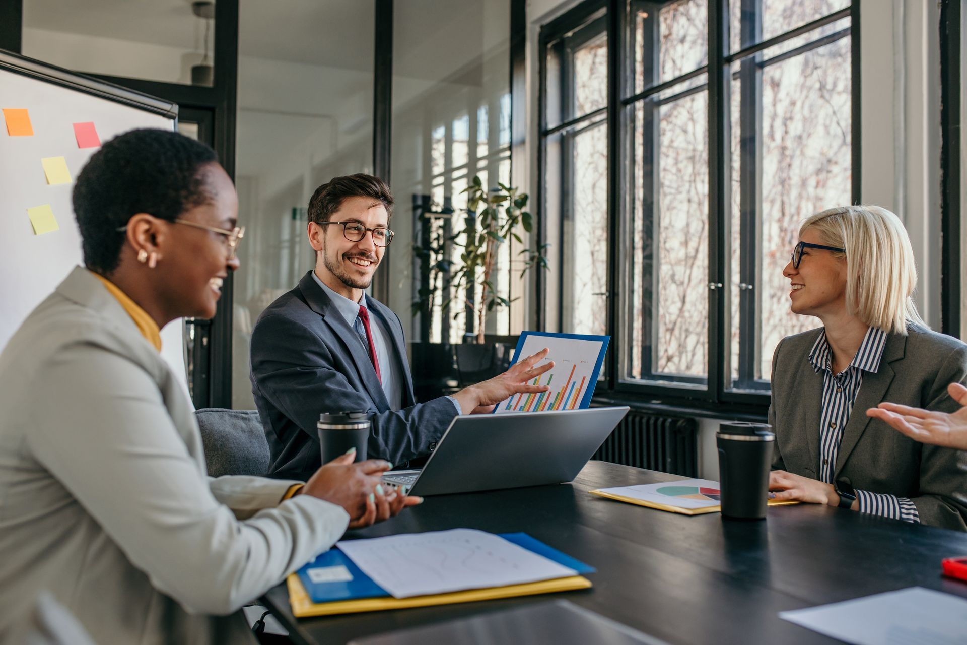 Three people in business attire in a meeting room, reviewing charts and smiling.
