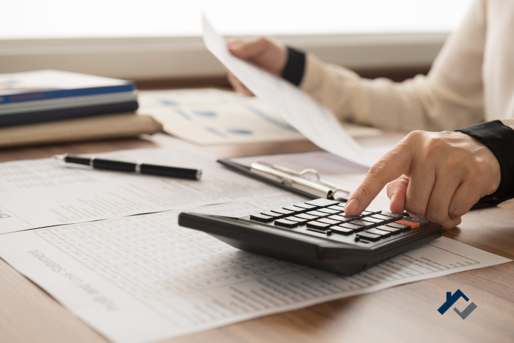 A desk with papers and person's hands with one hand pressing a button on a calculator.