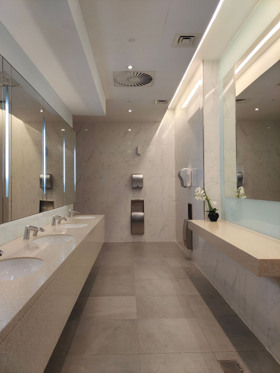 Modern restroom with long white sinks, mirrors, beige tiles, and a shower head overhead