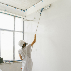 Person painting a white room ceiling with a roller near a window