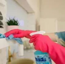 Person in pink gloves cleaning a bathroom faucet with a spray bottle and cloth.