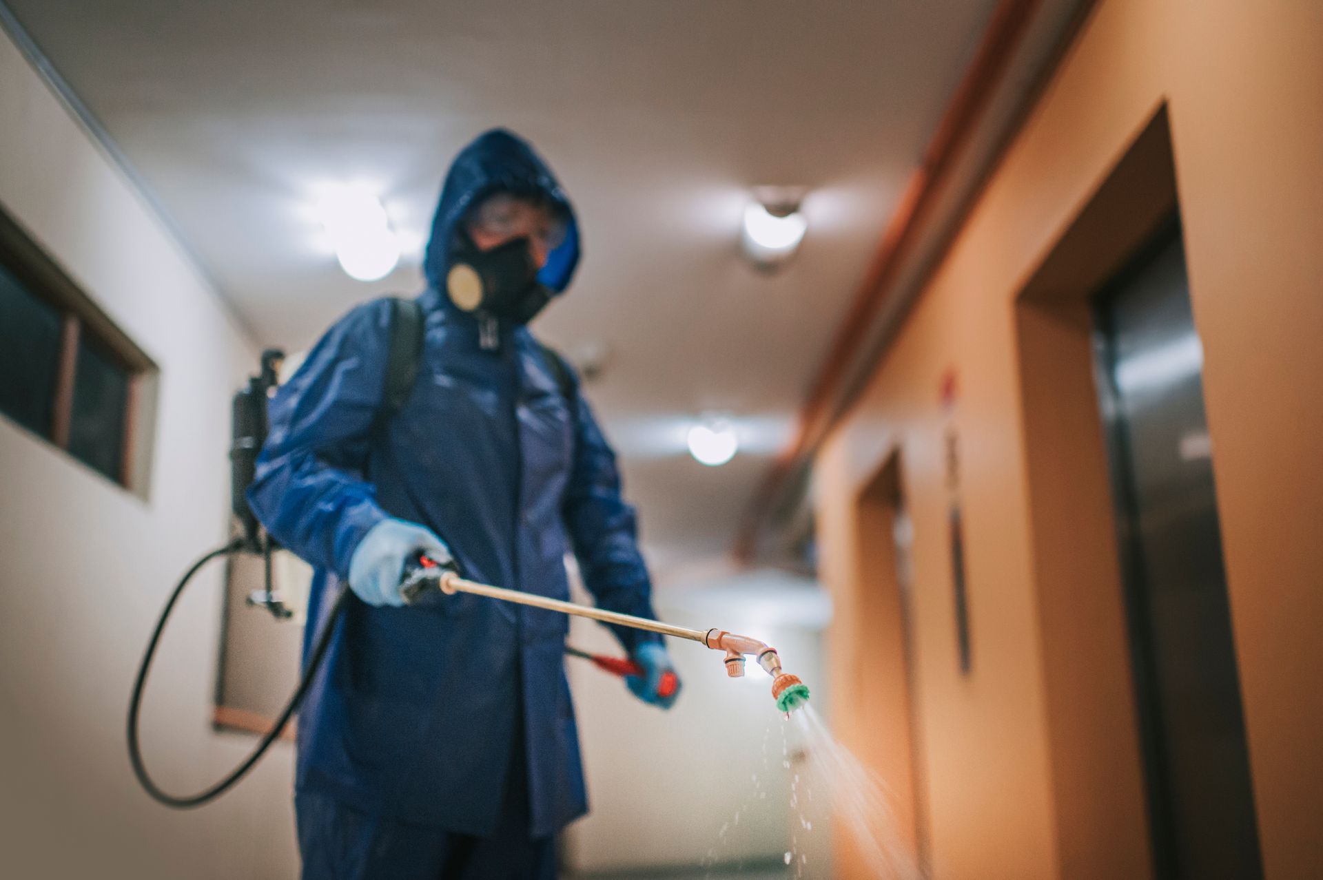 A man in a protective suit is spraying a hallway with a sprayer.
