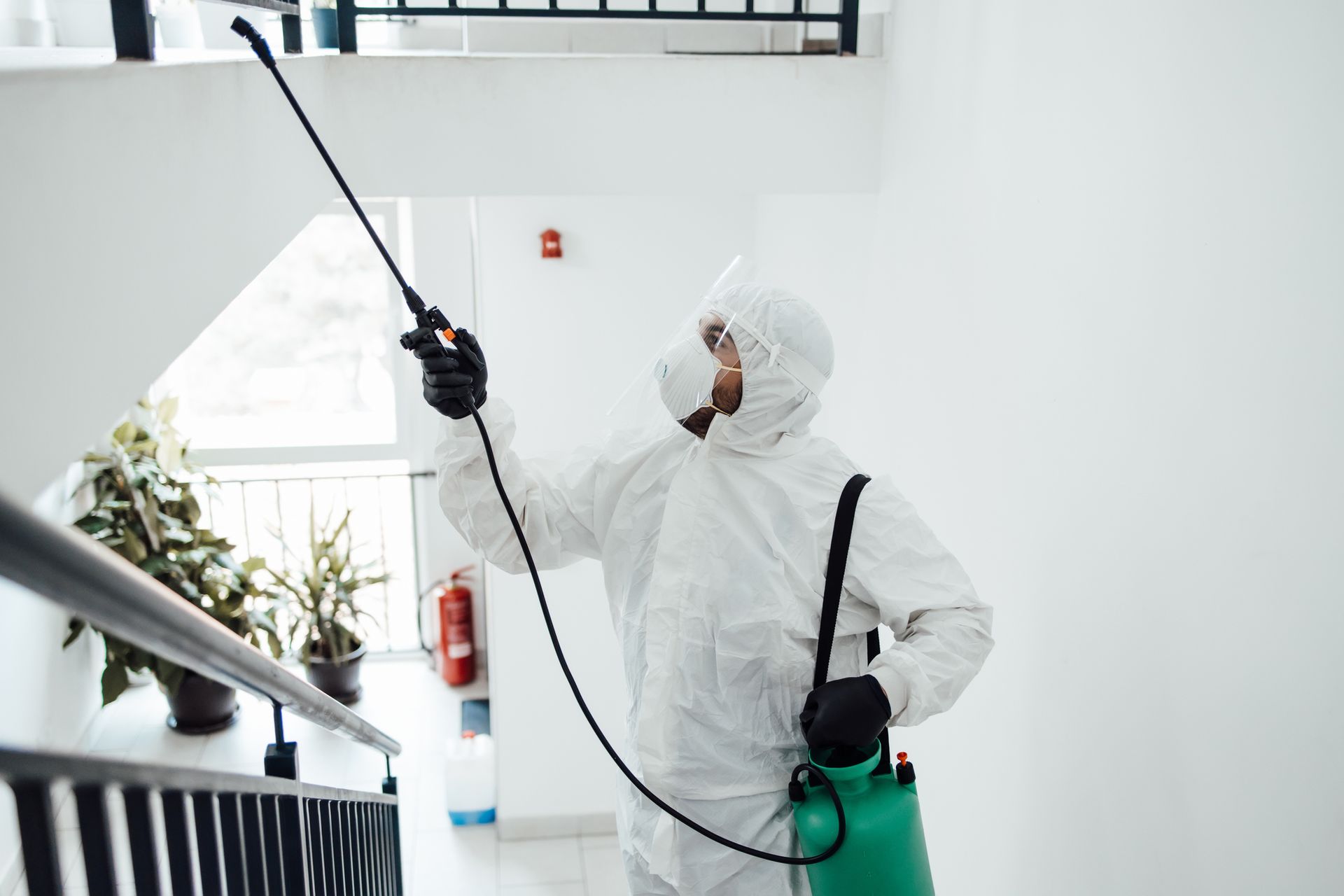 A man in a protective suit is spraying a room with a sprayer.