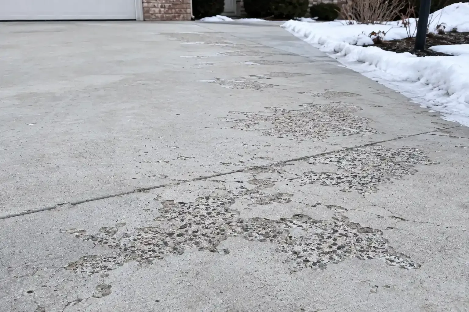 Flaking concrete driveway with dark patches and a house edge in the background