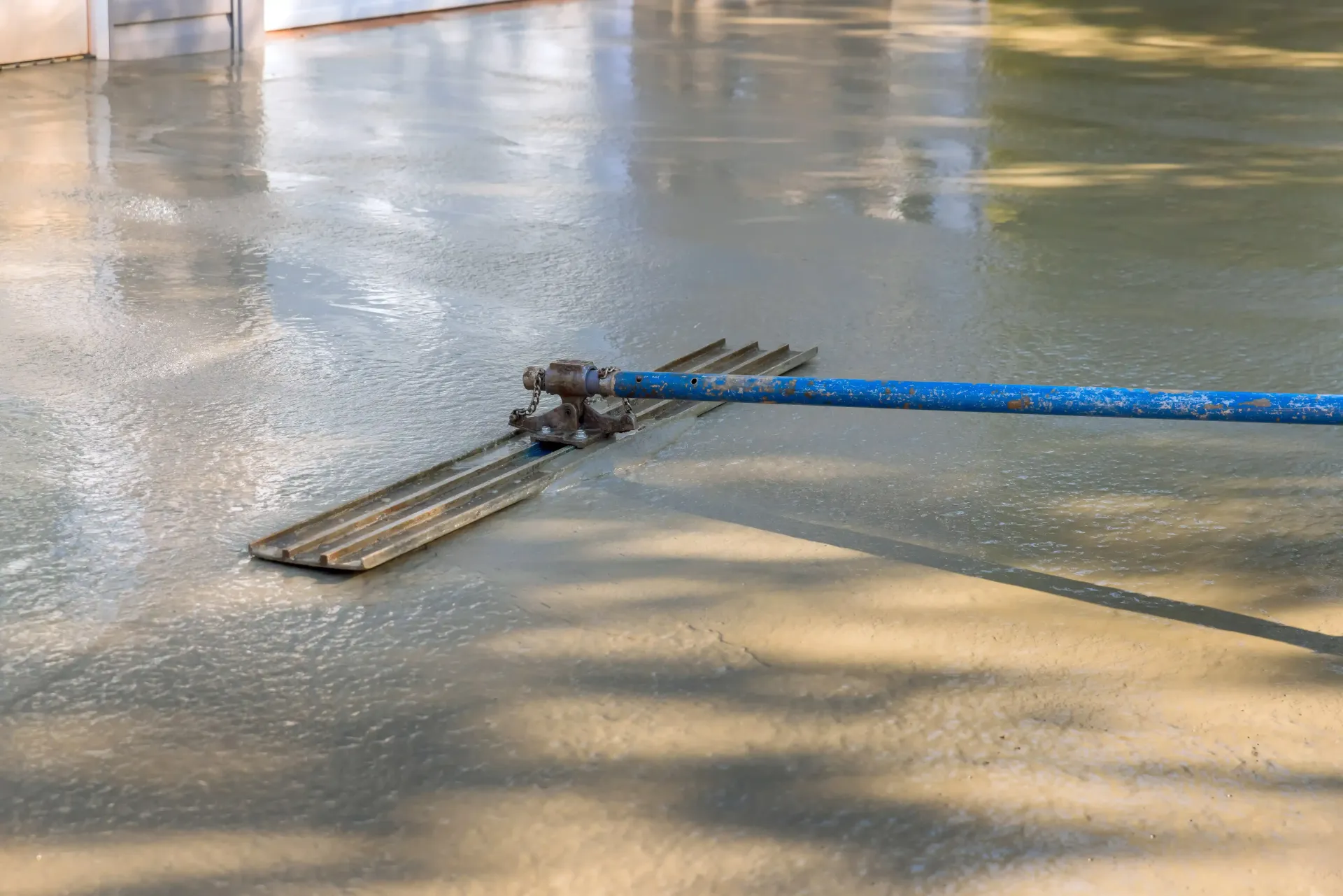 Blue squeegee on wet concrete floor in a warehouse or garage, with sunlight reflecting on the surface
