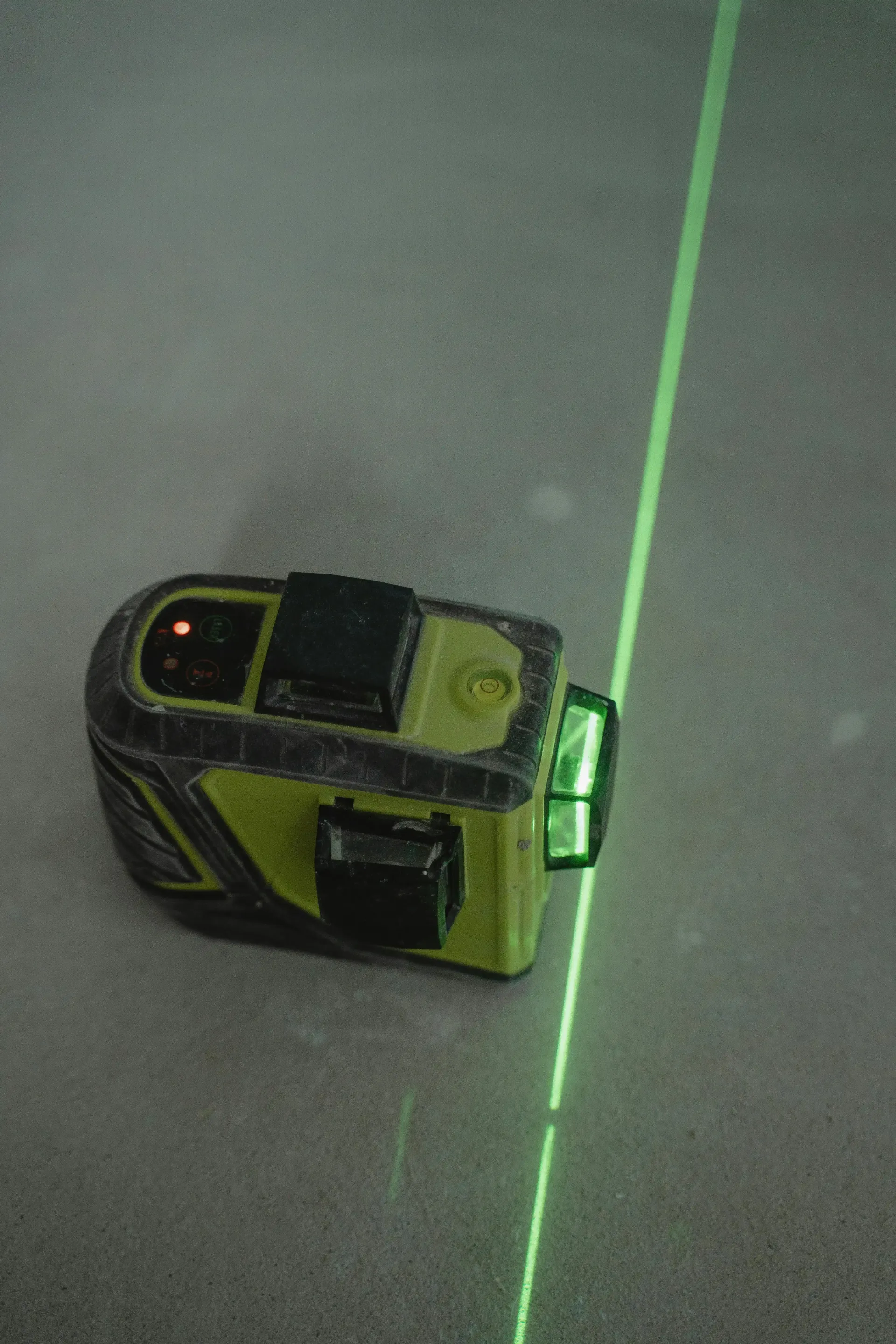 Yellow-and-black leveler crossing a glowing green line on a gray concrete surface