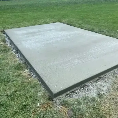 Freshly poured concrete slab in a grassy yard, viewed from an angle