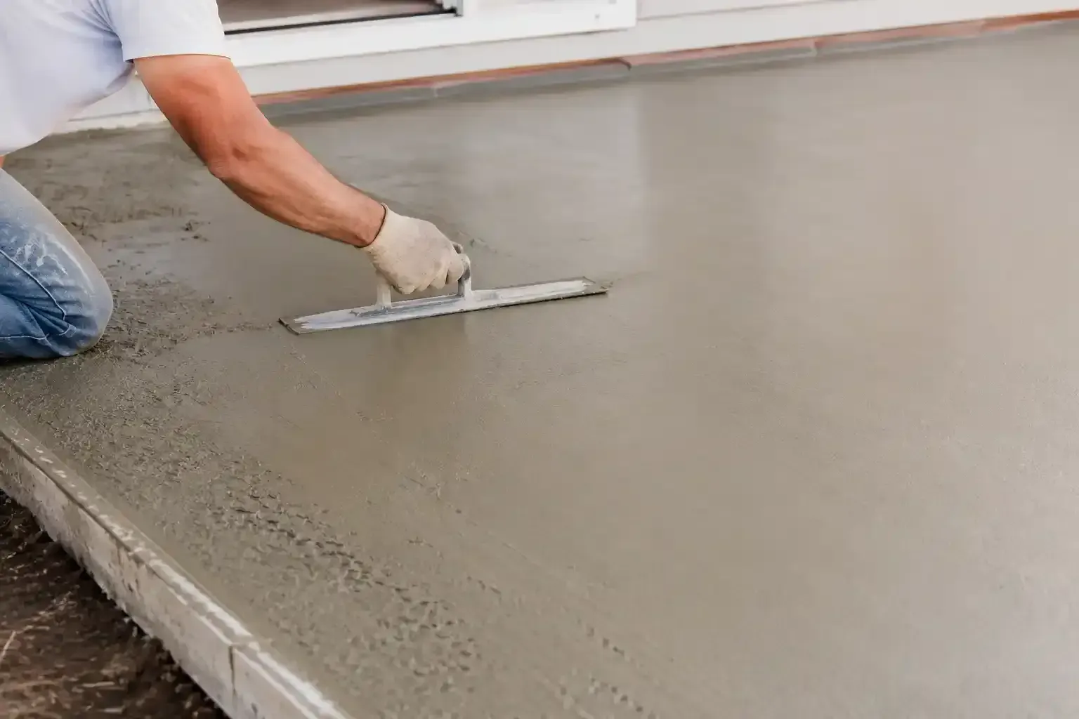 Worker smoothing wet concrete with a trowel on a freshly poured floor