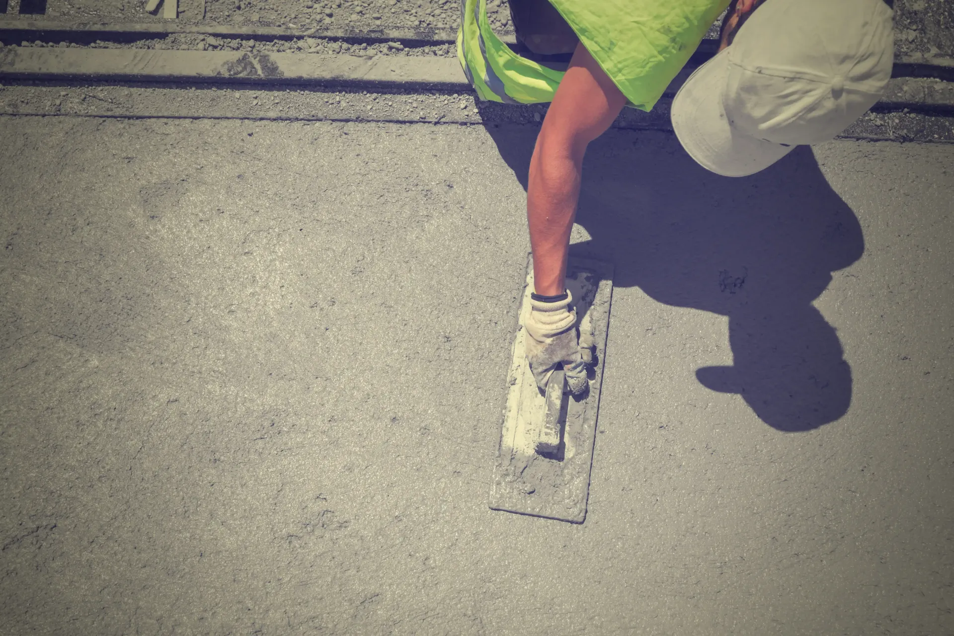 Worker smoothing new concrete wearing a white hat and green vest