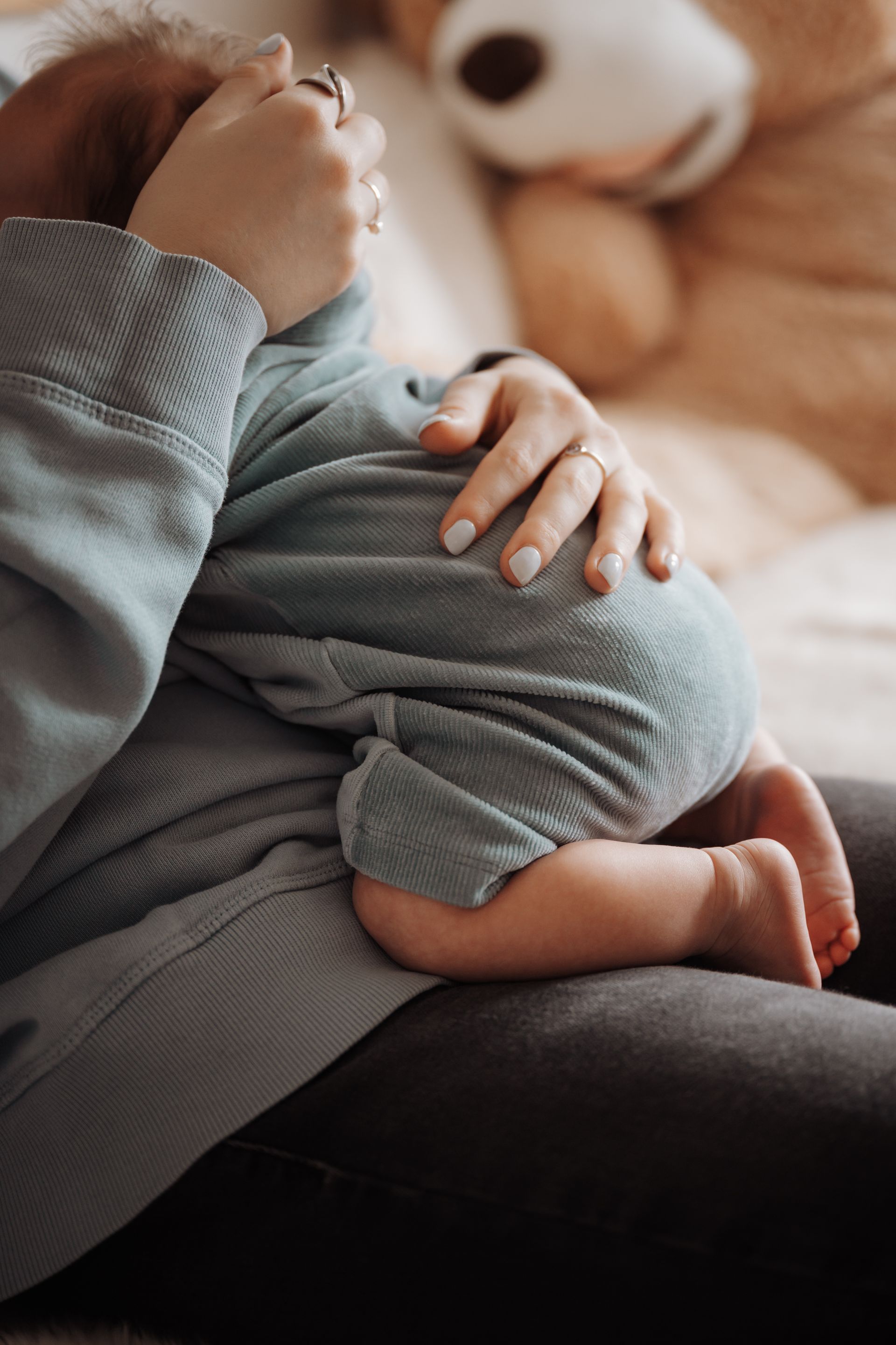Vrouw houdt slapende baby vast, vader kijkt toe; zachte verlichting, neutrale tinten.