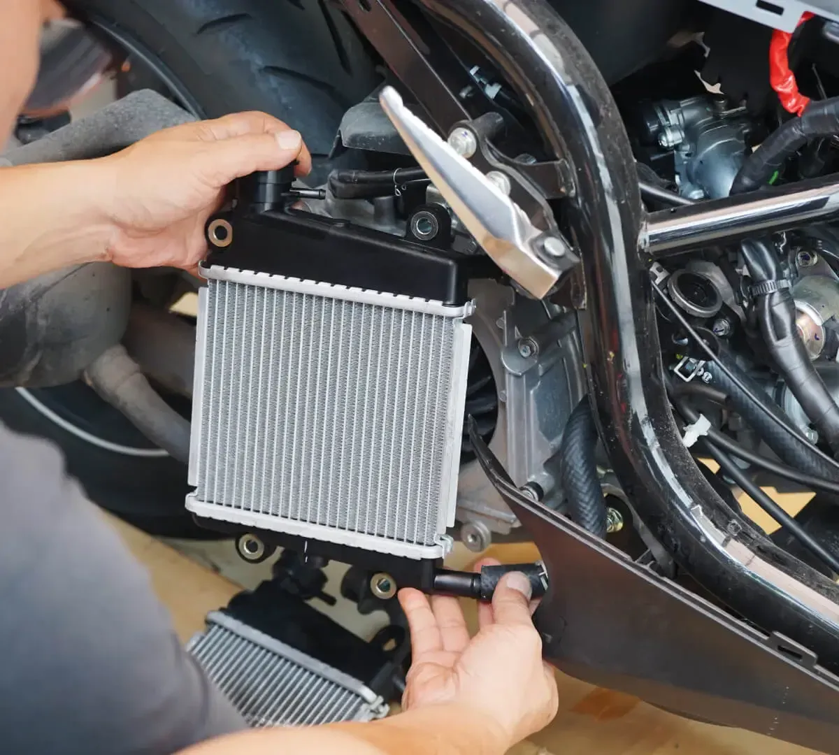 Mechanic installing a small radiator on a motorcycle frame in a garage