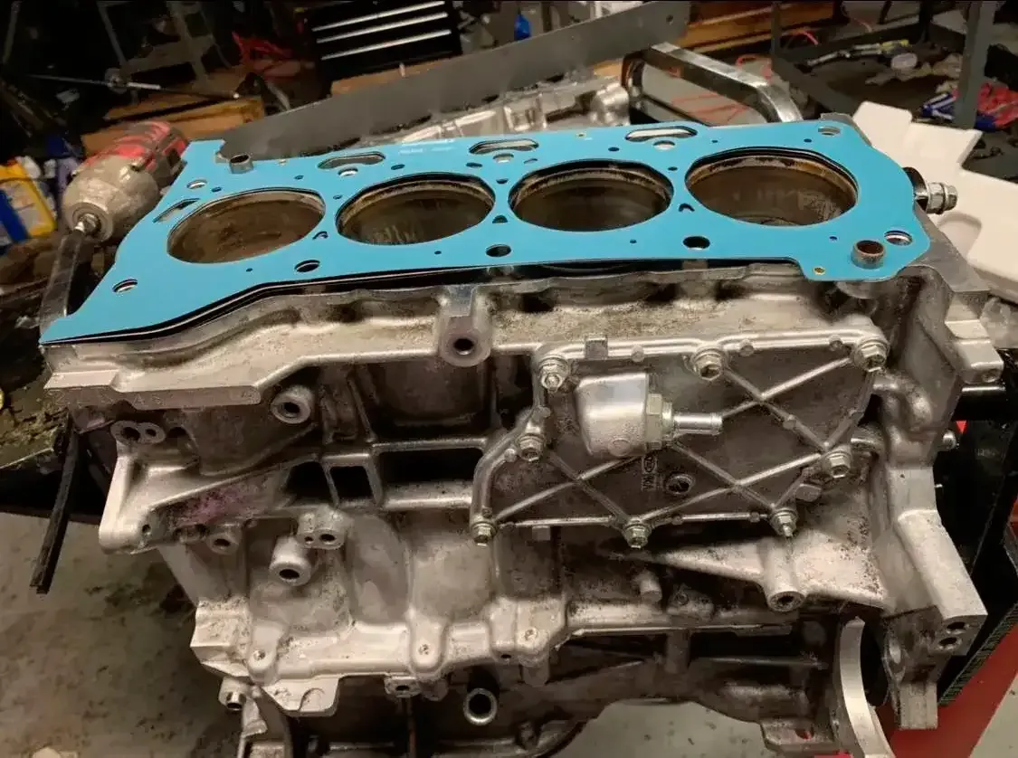 Car engine block with blue head gasket in a workshop, viewed from above