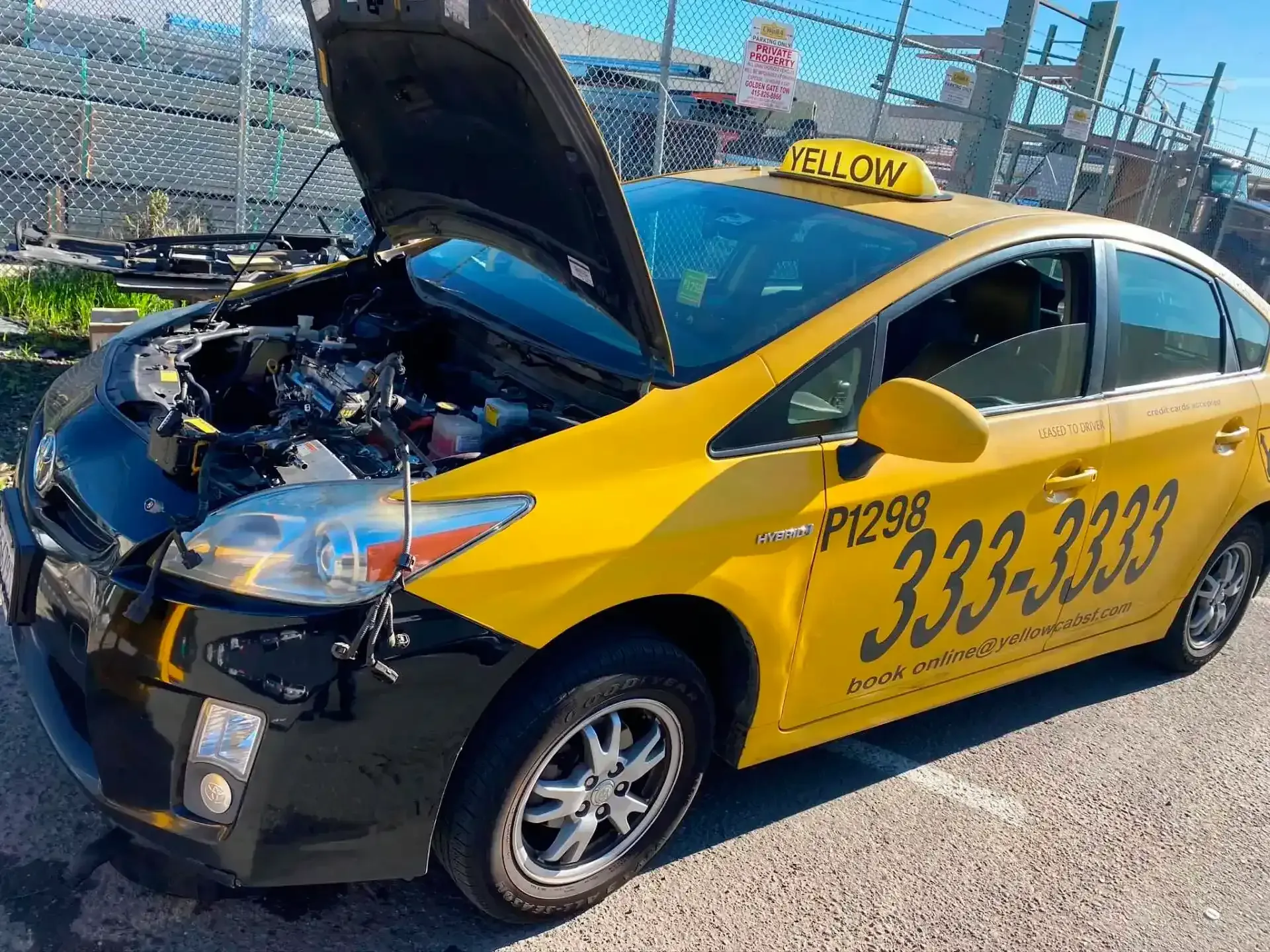 Yellow taxi with front-end damage and hood open on a street, shown at an angle