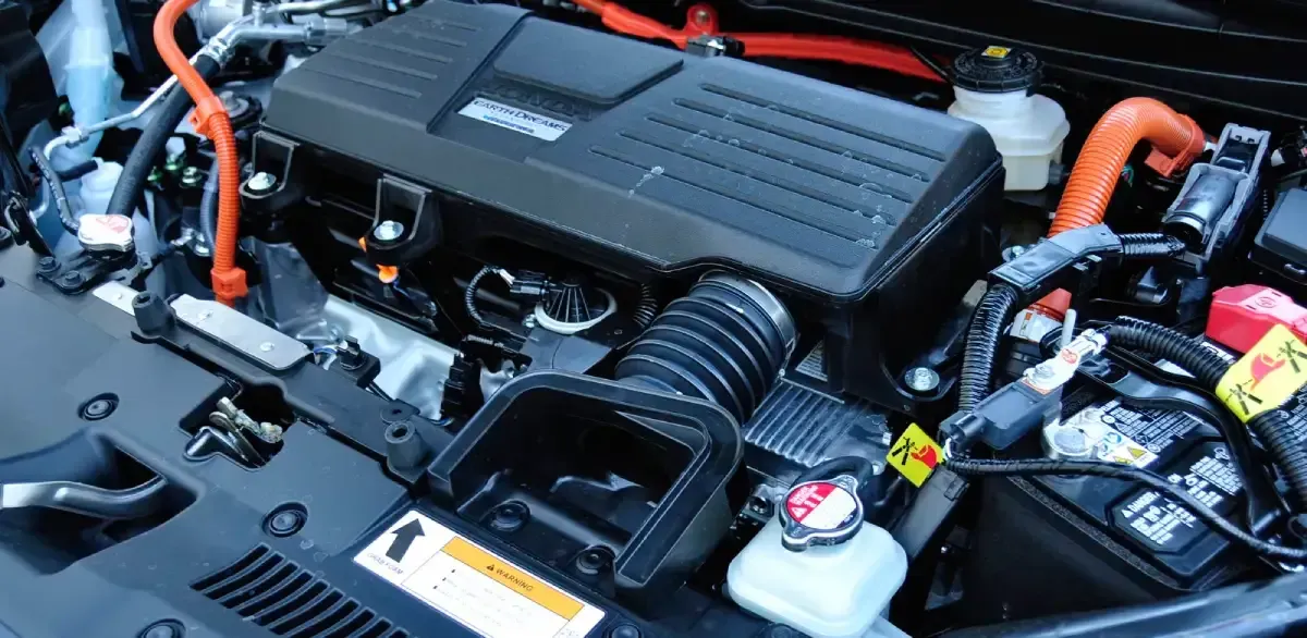 Close-up of a hybrid car engine bay with orange high-voltage cables and black engine cover