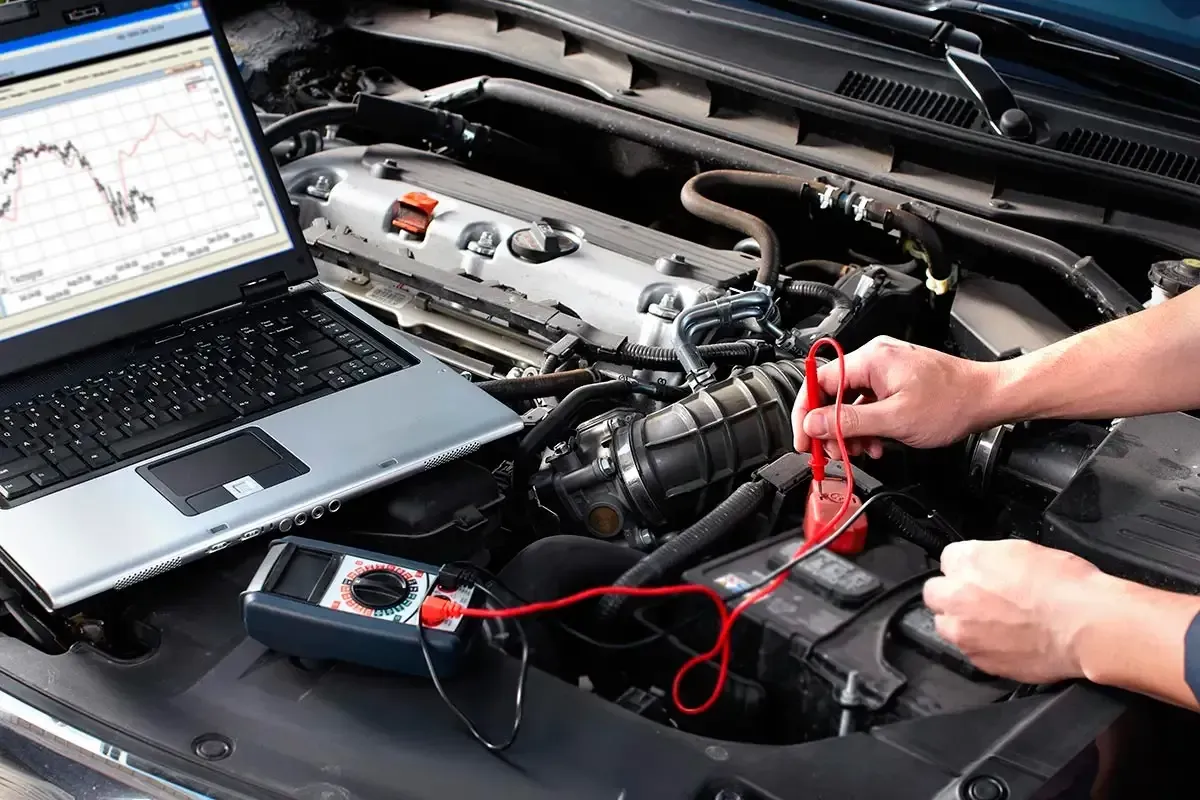 Person testing a car engine with a laptop and multimeter under the hood