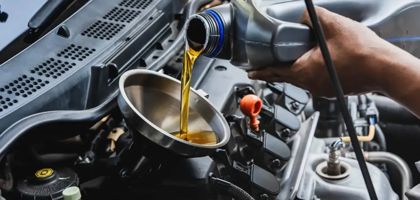 Engine oil being poured into a car’s open engine compartment during maintenance