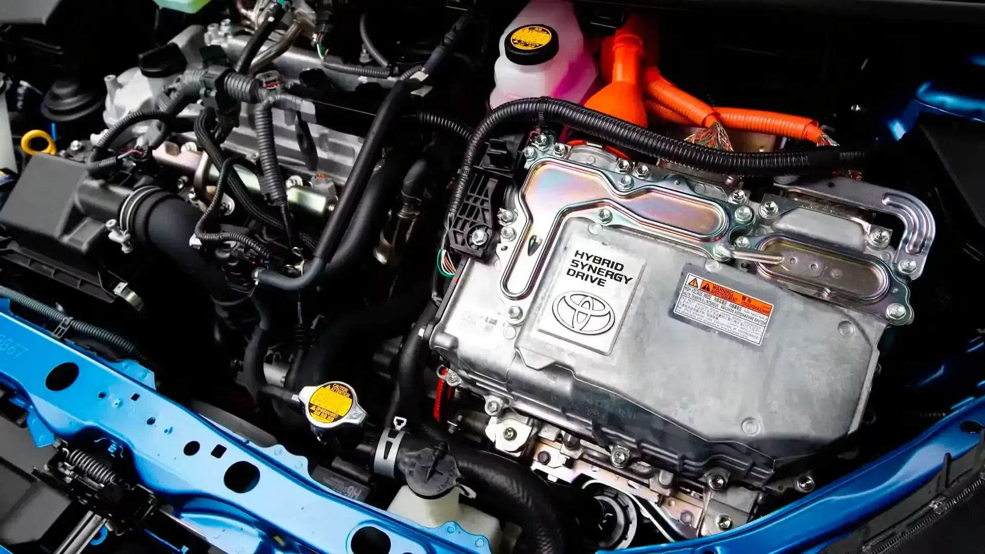 Car engine bay with exposed wiring, black components, and blue body panels under the hood